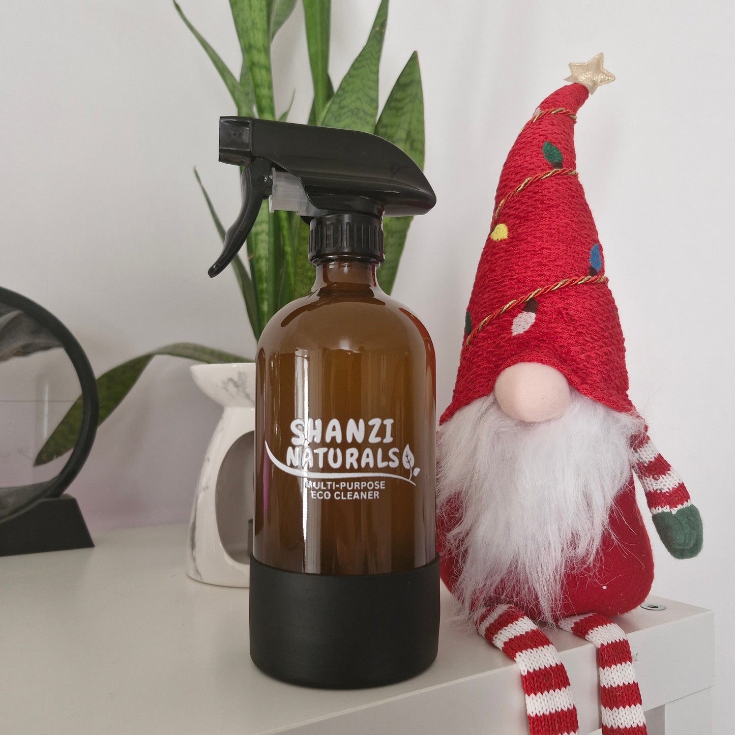 Shanzi Naturals bottle with a black spray nozzle on a white surface with a decorative gnome in the background.